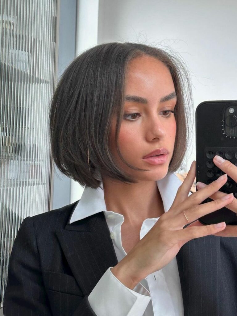 Woman taking selfie with smartphone, short hair, professional attire.